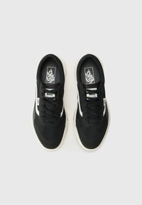 Sorte lerret sneakers med hvite detaljer, teksturert overflate, rund tå og flate snørebånd. Har en polstret såle og Vans-merke på tungen.