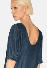 Denim-topp med dyp rygghals, korte pufferede ermer og mørkeblå vask. Særpreget sømmer langs kantene og ermene.