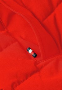 Tessuto trapuntato rosso con cuciture visibili e un piccolo interruttore o bottone cilindrico nero, bianco e rosso attaccato vicino a una cucitura.
