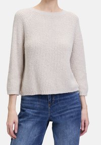 Light beige knitted sweater with a ribbed texture, three-quarter sleeves, and a relaxed fit, paired with blue denim jeans.