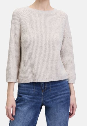 Lichtbeige gebreide trui met een ribbelstructuur, driekwartmouwen en een relaxte pasvorm, gecombineerd met blauwe denim jeans.