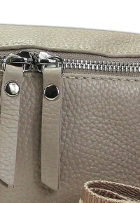 Beige nepleren tas met dubbele ritsen, metalen hardware-accenten en een gestructureerde buitenkant. Inclusief een stoffen schouderband.