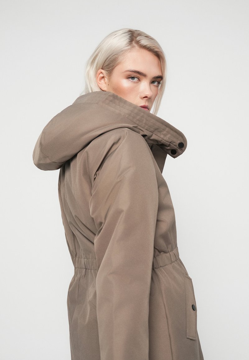 Brązowa, ocieplana parka z kapturem, elastycznym pasem, kieszeniami po bokach i zapięciem na guziki. Gładka tekstura z minimalistycznym designem.