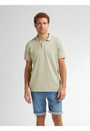 Polo shirt verde chiaro con rifinitura rosa al colletto, maniche corte e logo sul petto, abbinato a pantaloni shorts in denim arrotolati. Texture del tessuto liscia.