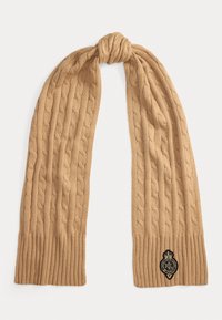 Sciarpa a maglia cable-knit in beige chiaro, con estremità a coste e un patch logo nero. Texture morbida con un design allungato e caldo.