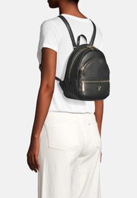 Sac à dos en cuir noir avec des garnitures dorées, sommet arrondi, double zip et poche avant. Porté sur le dos avec des bretelles réglables.