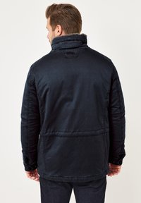 Marineblaue isolierte Jacke mit hohem Kragen, gerippter Struktur und knöpfbaren Manschetten. Verfügt über gestickte Akzente und eine glatte Oberfläche.