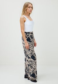 Vloeiende, high-waisted broek in een crème en marineblauw abstract patroon, gecombineerd met een aansluitend wit tanktop en zwarte schoenen. Glad materiaal.