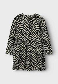 Garšīgu piedurkņu kleita ar melnbaltu zebrziņu rakstu, ar izplūdušu svārku un ribotām tekstūrām. Parādīts aizmugures skats.