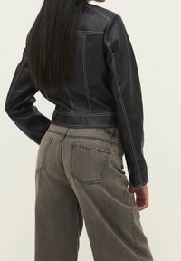 Black leather cropped jacket with white stitching, paired with high-waisted gray denim pants. Visible back pocket detail on pants.