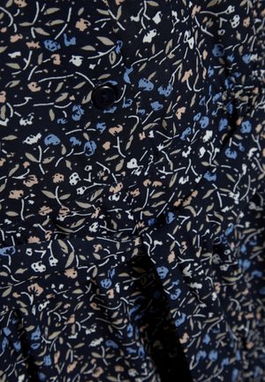 Nahaufnahme eines dunklen Stoffs mit kleinen Blumenmustern in Blau, Beige und Weiß, versehen mit einem schwarzen Knopf und einem gerafften, gerafften Detail.