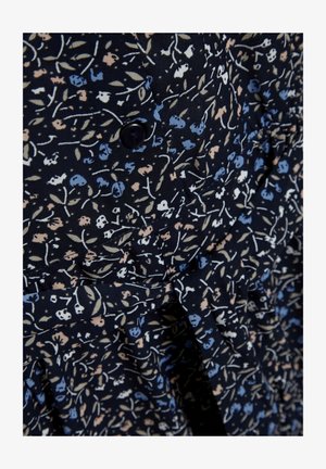 Nærbilde av mørkt stoff med små blomstertrykk i blått, beige og hvitt, med en svart knapp og rynket, volangdetalj.