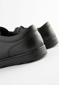 Schwarze Lederschuhe mit glatter Oberfläche, runder Form und einer strapazierfähigen Gummisohle. Sichtbare Stitching-Details entlang der Seiten.