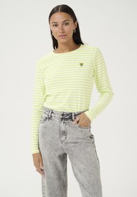 Lange mouwen gestreepte shirt in lichtgroen en wit, met een klein hartembleem. Gecombineerd met hoge taille grijze denim jeans.
