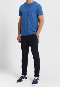 Blå bomulls t-shirt med korta ärmar och bröstficka, tillsammans med mörkblå byxor och blå sneakers med vita detaljer.