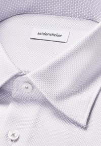 Camicia bianca a maniche lunghe con texture a spina di pesce, con un colletto impeccabile e un'etichetta con la scritta "seidensticker."