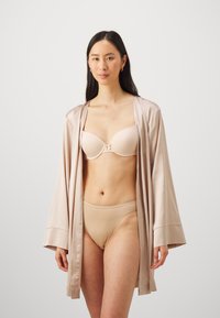 Satin kimono gaisā beigus krāsā, kas drapēta pāri kailai krūštura un atbilstošu biksīšu komplektam, uzsverot gludu tekstūru un vienkāršu dizainu.