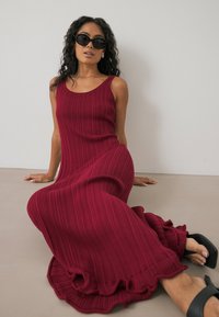 Geribbelde, bordeaux maxi-jurk met een uitlopende zoom en ruches. Gladde stof, mouwloos ontwerp. Zwarte blokhakken mules maken de look compleet.