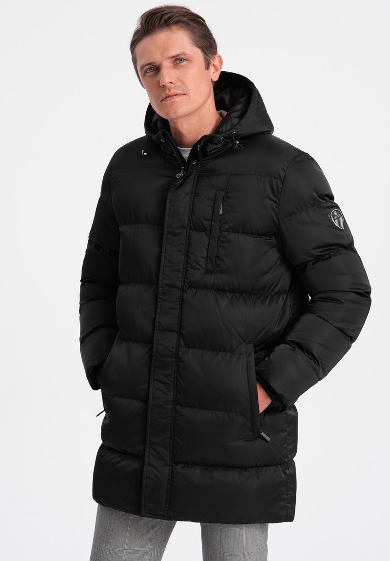 Cappotto imbottito nero con cappuccio, dotato di zip frontale e chiusura a bottoni, tasche laterali e tasca sul petto. Design trapuntato texturizzato.