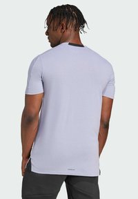 Camiseta de manga corta de color púrpura claro con cuello redondo, presenta aberturas laterales, acentos negros cerca del cuello y la marca "AEROREADY" en el dobladillo trasero.