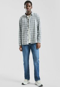 Koszula zapinana na guziki w szaro-białą kratę, noszona na jasnym T-shircie, w połączeniu z niebieskimi dżinsami i białymi tenisówkami. Prosty, codzienny wygląd.