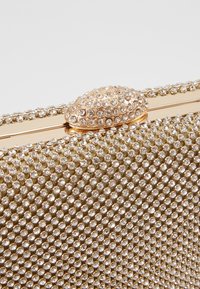 Borsa a mano dorata ricoperta di piccoli strass lucenti, con una chiusura testurizzata dal design arrotondato e una finitura metallica liscia.