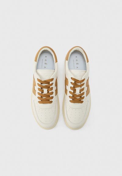 Ζευγάρι λευκά και καφέ δερμάτινα sneakers με καφέ κορδόνια, διάτρητη περιοχή στα δάχτυλα και επώνυμα εσωτερικά πέλματα σε ανοιχτό φόντο.