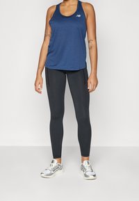 Granatowy top sportowy na ramiączkach i czarne legginsy o strukturalnym wykończeniu, wraz z srebrnymi butami sportowymi z białymi akcentami i masywną podeszwą.