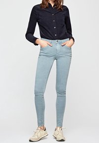 Vaqueros ajustados de color azul claro con una textura suave y cierre de botón, combinados con una camisa de botones azul marino oscuro y zapatillas beige.