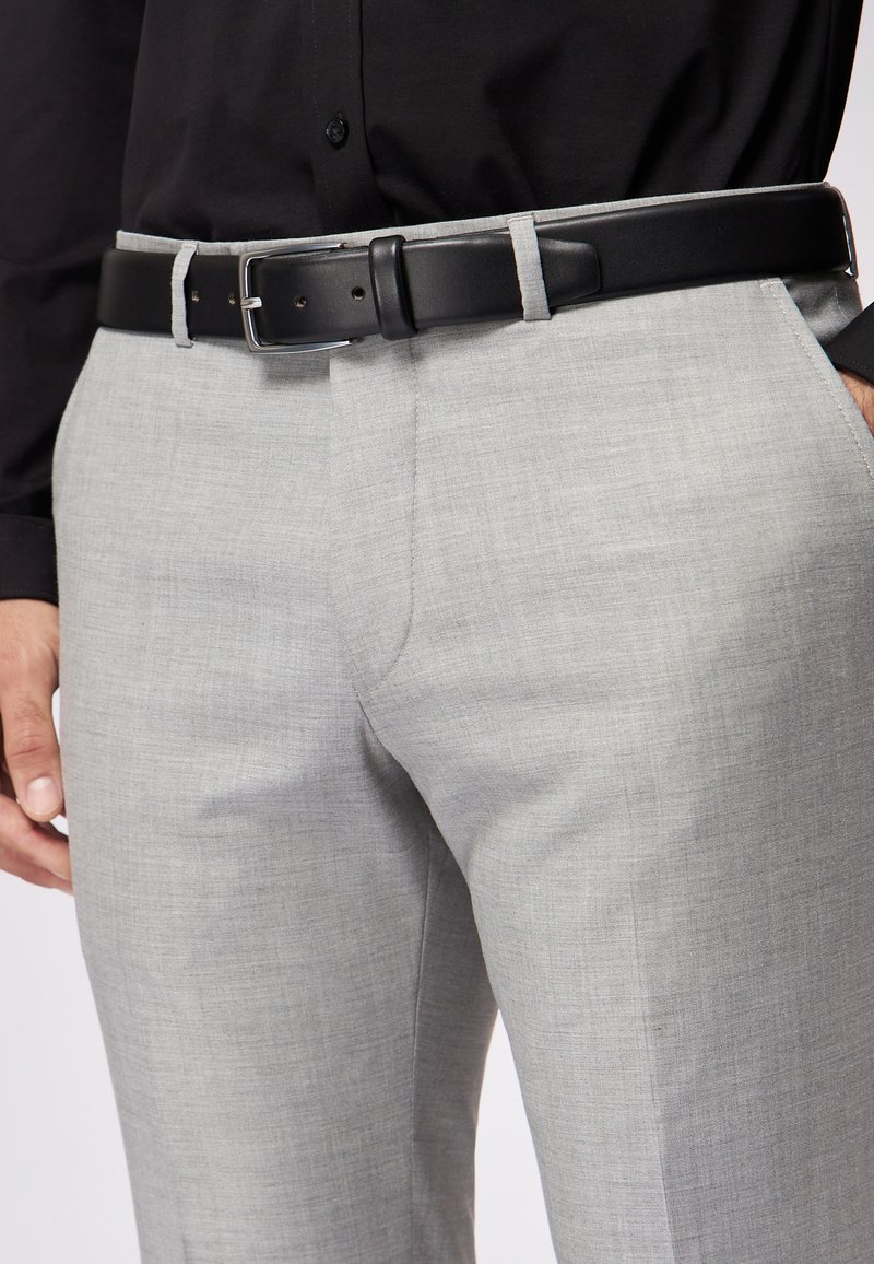 Lichtgrijze op maat gemaakte broeken met een subtiele textuur, gecombineerd met een zwarte leren riem met een vierkante zilveren gesp.