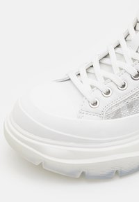 Białe sneakersy z teksturowanej skóry i siateczkowego wierzchu, gumowa podeszwa z przezroczystymi sekcjami, okrągły czubek i sześć oczek do sznurowania.