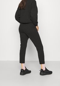 Svart quiltad träningsdress med långa ärmar och kortat fåll, tapered byxor och svarta sneakers. Strumporna har rosa med oranga randiga accenter.