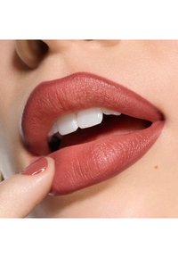 Matte mauve läppstift applicerat på fylliga, släta läppar, som framhäver en neutral färgton och naturlig glans. Vita tänder synliga.