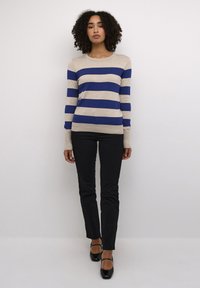 Striped sweater with wide blue and beige stripes, round neckline, and long sleeves, paired with black fitted pants and black heeled shoes.