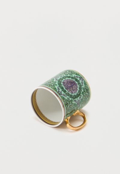 Πορσελάνινο φλιτζάνι τσαγιού με πράσινο και μοβ λουλουδένιο μοτίβο και χρυσή λαβή, ξαπλωμένο στο πλάι σε λευκή επιφάνεια.