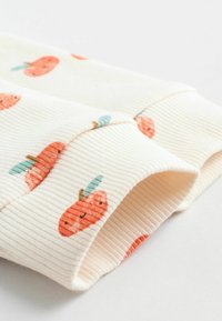 Rippstoff in Creme mit kleinen orangefarbenen Kürbis-Motiven und türkisfarbenen Blättern. Verfügt über eine weiche Textur und hochgerollte Säume.