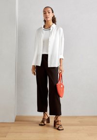 Hvit skjorte med knapper, svarte cropped bukser, svarte strappy hæler og en liten rød vevd håndveske. Glatt stoff, avslappet passform, moderne utseende.