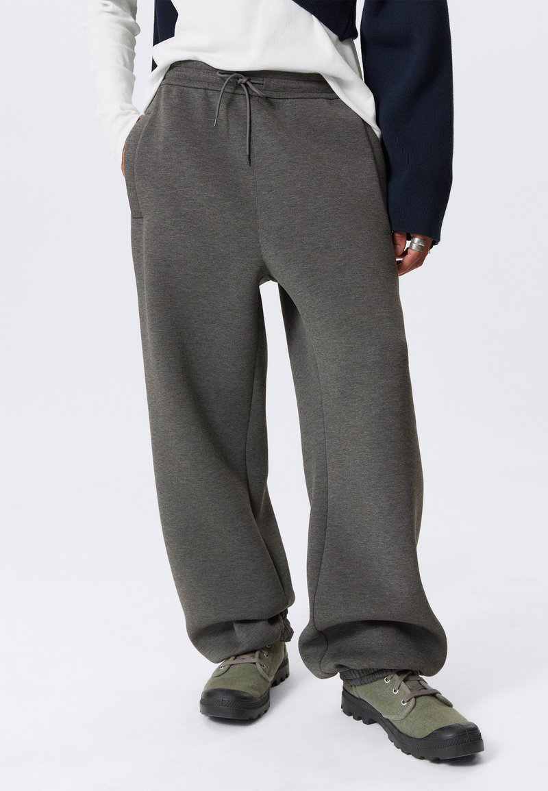 Graue Sweatpants mit bequemem Schnitt, Kordelzugbund und seitlichen Taschen, kombiniert mit grünen Low-Top-Schuhen und strukturiertem Stoff.