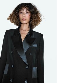 Schwarzer zweireihiger Blazer mit Satinrevers und Taschenakzenten. Verfügt über große Knöpfe und eine glatte Stoffstruktur.