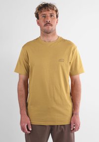 T-shirt en coton jaune avec col rond et manches courtes ; présente un petit logo "Oxbow" de couleur sombre sur la partie gauche de la poitrine.