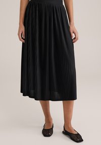 Svart plisserad midikjol i lätt tyg med skarpa vertikala veck. Matchad med svarta vävda ballerinas som har en minimalistisk design.