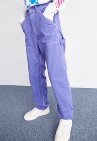Lavender cargo pants with a loose fit, featuring contrast stitching, side pockets, and a smooth cotton texture, paired with white sneakers.