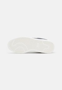 Sole of a sneaker featuring a white rubber material with a hexagonal patterned texture. Shaped with a slight curvature for grip.