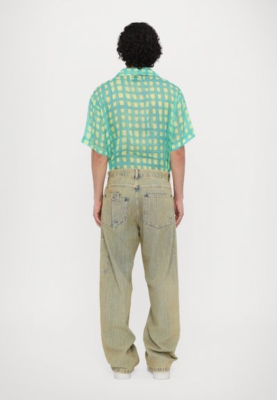 Short-sleeve shirt in light turquoise with yellow grid pattern, paired with loose-fitting, light-colored denim pants and white sneakers.