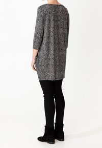 Túnica de estampado paisley en blanco y negro con mangas de tres cuartos, combinada con pantalones negros ajustados y botas negras.