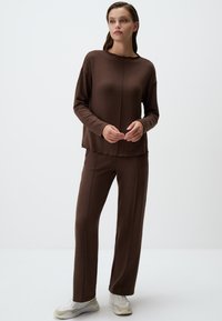 Brauner Strickpullover mit langem Arm und rundem Halsausschnitt, kombiniert mit passenden weit geschnittenen Hosen. Der Stoff hat eine glatte, weiche Textur und minimale Nähte.