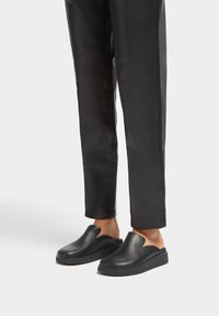 Black slip-on shoes with a curved cutout design, made of smooth leather, featuring a thick sole and minimal tread texture.