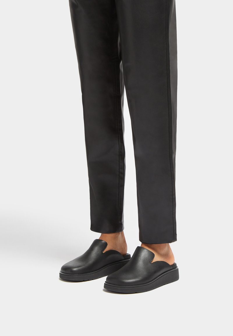 Black slip-on shoes with a curved cutout design, made of smooth leather, featuring a thick sole and minimal tread texture.