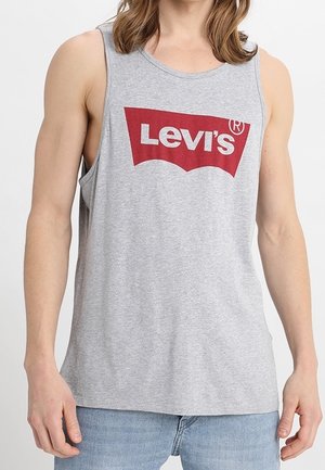 Mężczyzna w szarym bezrękawniku Levi’s z czerwonym logo, w jasnoniebieskich dżinsach, przedstawiony od ramion do bioder.