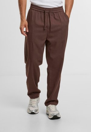 Brown sweatpants with an elastic waistband, front pockets, and a relaxed fit, paired with silver running shoes.
